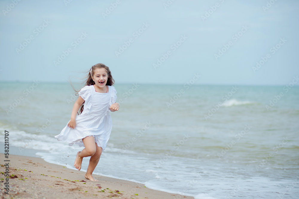 Cute little girl running along the seashore against a clear blue sea and rejoices