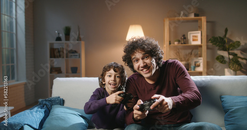 Funny south asian siblings are relaxing together, playing video games in front of tv, father and son expressing emotions while enjoying their hobby - family time concept  © andreybiling