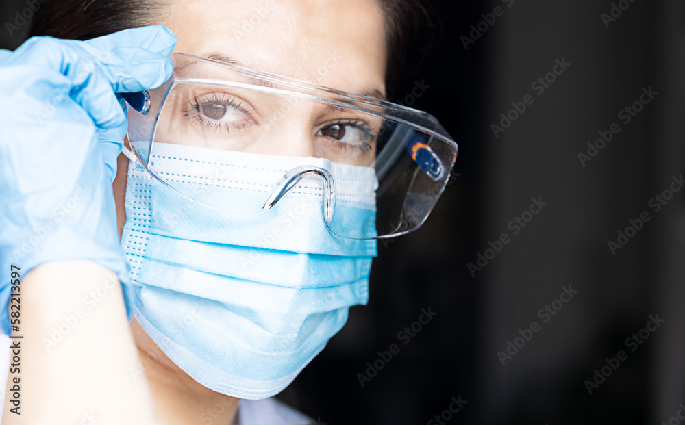 Portrait of a woman, nurse or doctor, with protective equipment, blue latex gloves, surgical mask and protective glasses. Concept of medicine, health protection from doctors, pandemics, viruses