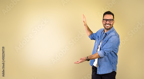 Billede på lærred Portrait of smiling young adult man wearing blue denim shirt and eyeglasses gest