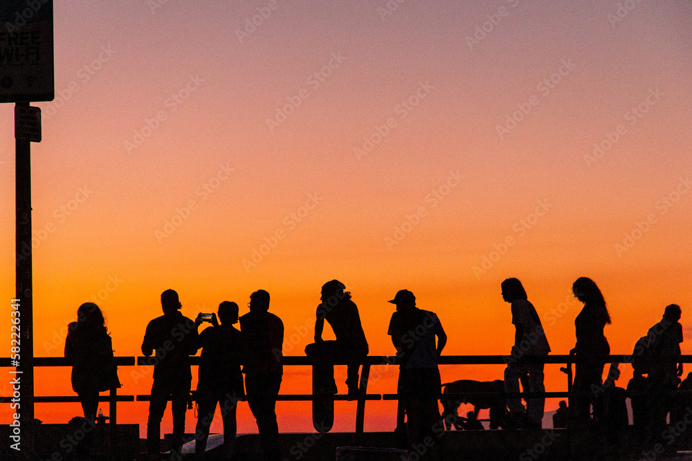 Fototapeta premium silhouettes of people watching the skateboarders at the venice beach skate park during sunset in california.