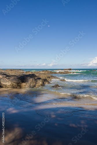 beach and rocks and the sea with waves transparent water clouds on the sky