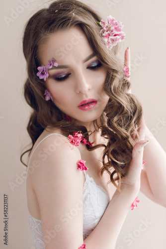 Cosmetics and manicure. Close-up portrait of attractive woman with dry flowers on her face and hair, pastel color, perfect make-up and skin on blue background. Fresh, trendy, spring retouched portrait