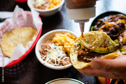 Hot sauce being added to a fajita on a corn tortilla in a mexican restaraunt