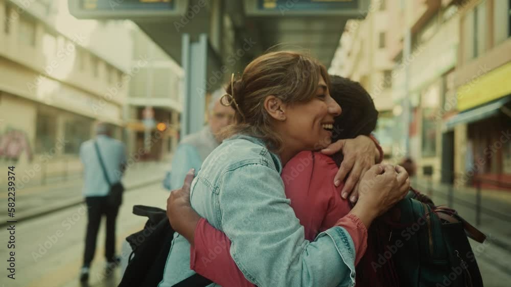 Happy multiracial women hugging while waiting at the bus station Happy multiracial women hugging while waiting at the bus station