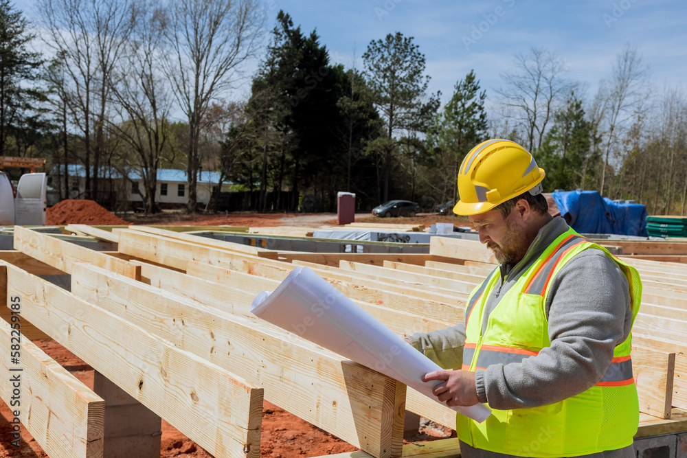 Building engineer with extensive experience holding in his hands blueprint project monitoring progress of construction as it occurs Building engineer with extensive experience holding in his hands blueprint project monitoring progress of construction as it occurs