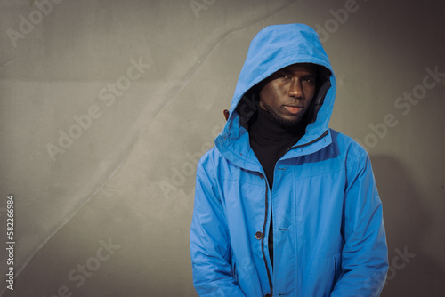 A young handsome african man in blue hooded jacket with dark gray background with blank area for writing 