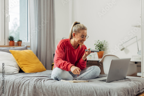 A beautiful blonde woman is sitting on the bed and talking on the phone