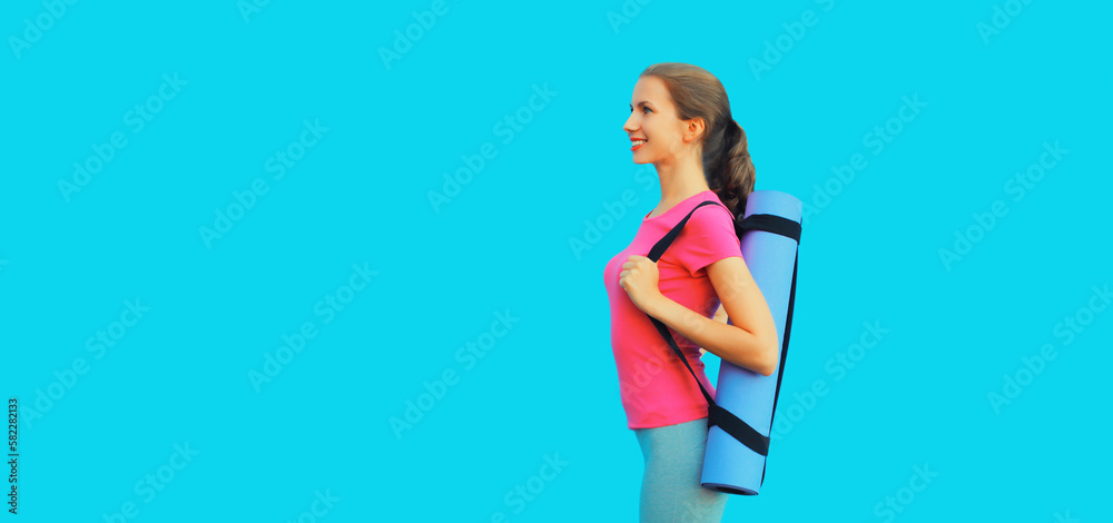 Sport and fitness concept - portrait of happy smiling young woman in sportswear with yoga mat on blue background Sport and fitness concept - portrait of happy smiling young woman in sportswear with yoga mat on blue background