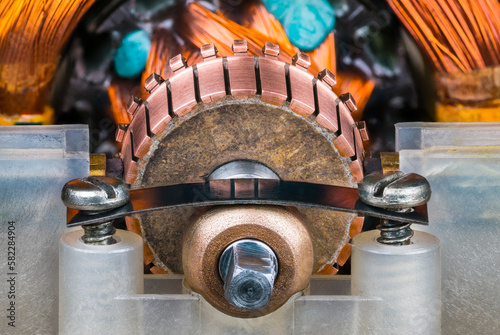 Closeup of commutator copper segments and plain bearing bronze housing in plastic pillow block. Steel flat leaf spring with screws inside old blender electric motor with rotor and stator wire winding.
