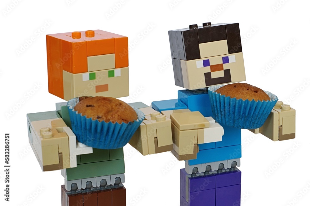 Obraz premium LEGO Minecraft large figures of Steve and Alex holding small baked muffins placed in blue paper cups. White backgound