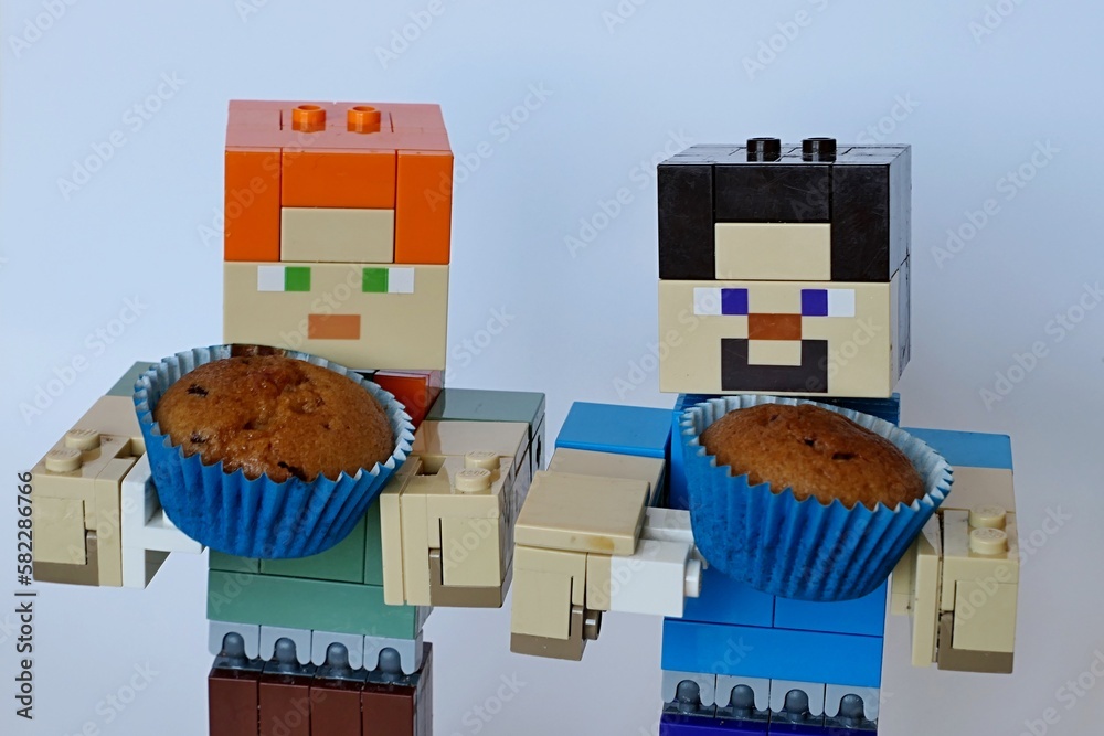 Fototapeta premium LEGO Minecraft larger figures of Steve and Alex, both holding small, bronze baked muffin cupcake in a blue paper cup.