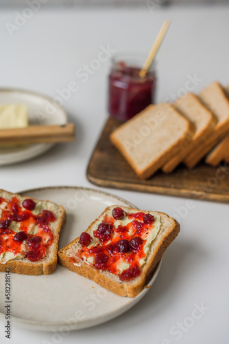 Bread with butter and cranberry jam is on the table and ready to eat. A delicious and sweet breakfast. Aesthetically pleasing serving of food. Recipe for toast with butter and jam.