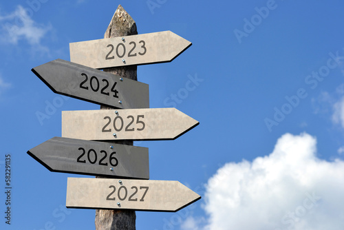 2023, 2024, 2025, 2026, 2027 - wooden signpost with five arrows, sky with clouds © PX Media