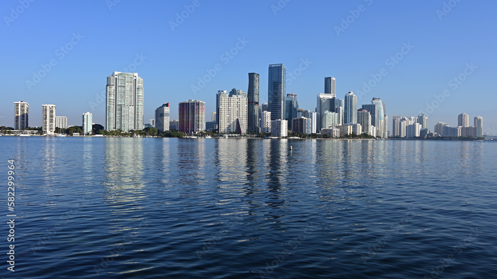 Miami, Florida skyline reflected on calm Biscayne Bay in morning light on sunny clear day.