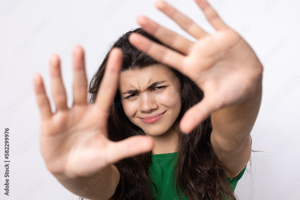 Portrait of a serious young woman showing stop gesture with her palm over white background