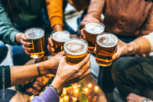 Group of friends drinking and toasting glass of beer at brewery pub restaurant- Happy multiracial people enjoying happy  hour with pint sitting at bar table- Youth Food and beverage lifestyle concept