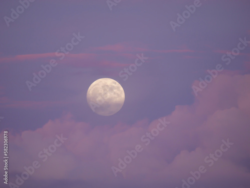 Dreamy moment of a big rising full moon above pink colored cloud in a blue sky