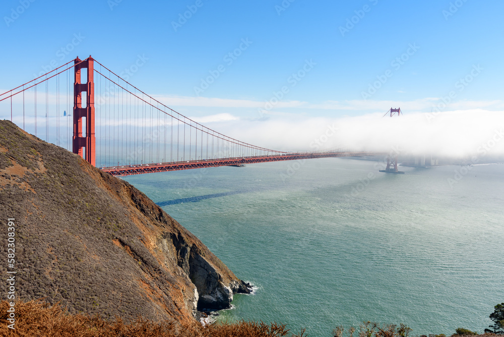 View of Golden Gate bridge partially covered with fog drifting from the ocean on a fall morning View of Golden Gate bridge partially covered with fog drifting from the ocean on a fall morning