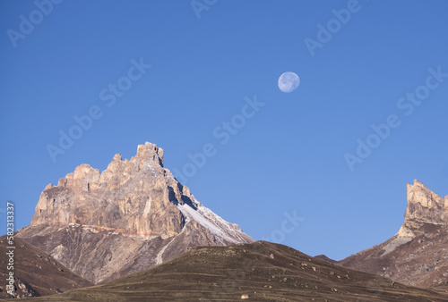 The waning moon in the mountains against the background of a blue sky with rocks and mountains, autumn in the mountains