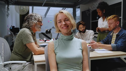 Smiling blonde Caucasian blonde business woman looking at camera sitting in office. Executive CEO female professional manager posing for entrepreneur portrait. Happy people at their work station.  photo