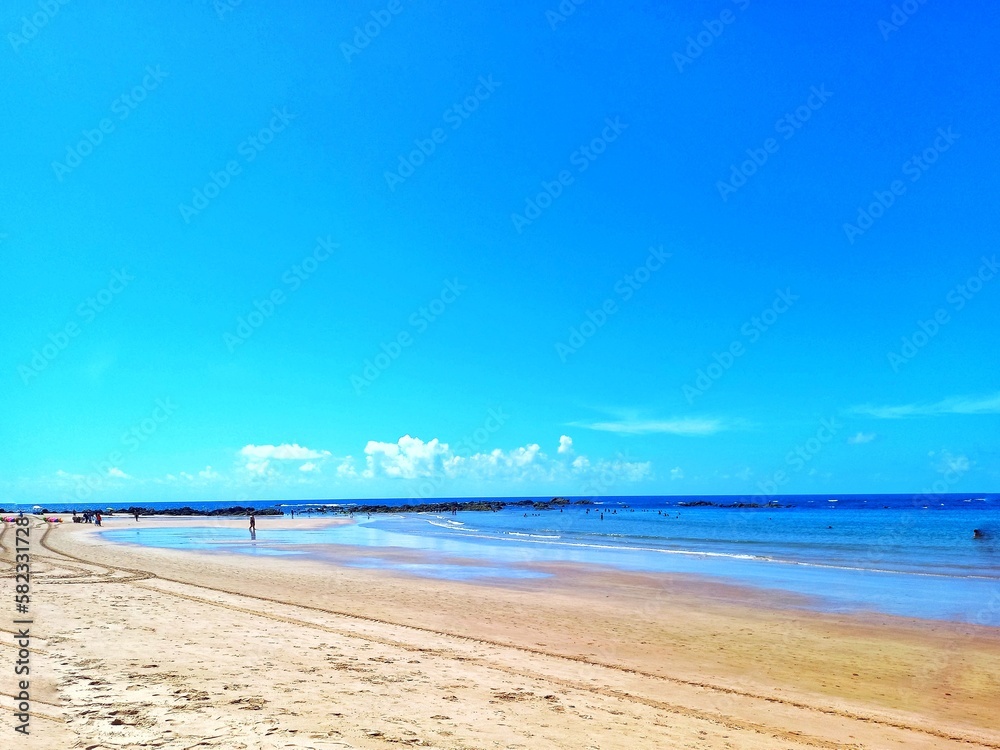 Beautiful Piatã Beach, Salvador, Bahia, Brazil on a summer morning. Fresh air, gentle wind, blue sky with few clouds, low tide, people walking in the distance.