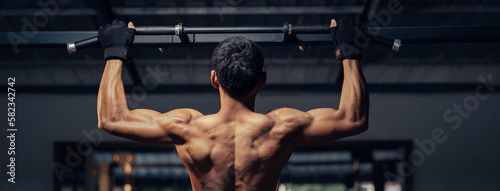 Athletic pulling up showing back muscle at gym. Muscular man exercise pull up on bar in fitness gym. Bodyweight workout. Banner ratio. photo