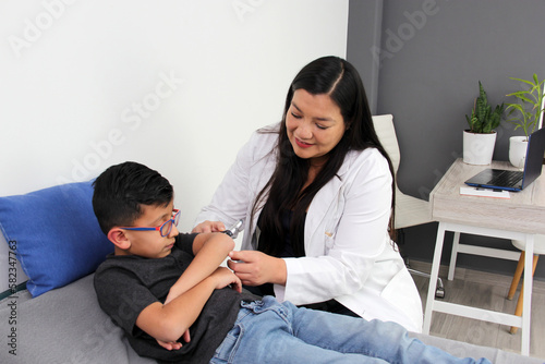 Latina female pediatrician doctor attends to her 6-year-old boy patient, checks her fingers, hands, wrist, arm and elbow for pain or injuries