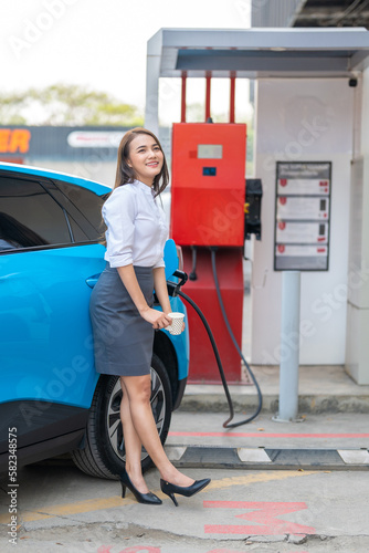 Woman standing holding a cup of coffee while waiting to charge an electric car at a city public charger station