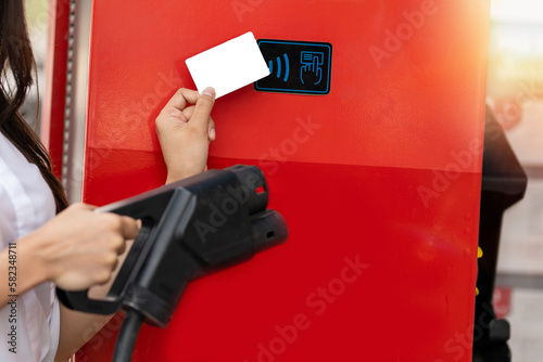 Billede på lærred Hand holding calltime refill card or prepaid card to refill money of charging electric car ( EV ) machine at charging station with nature background