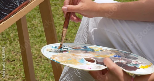 Close-up of a brush in a woman's hands picking up acrylic paint on a palette for drawing. Creativity and hobby concept.