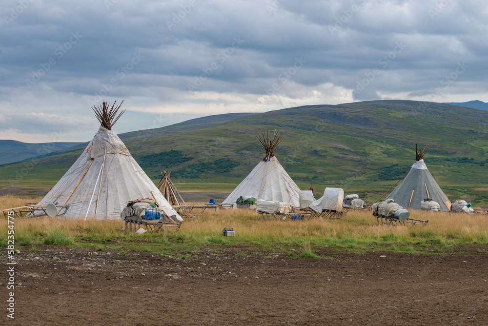 Three wigwams of modern reindeer herders against the background of the foothills of the Polar Urals on a cloudy August day. Yamalo-Nenets Autonomous Okrug, Russia