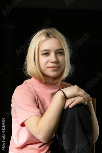 Studio portrait of a young beautiful blonde girl in a pink t-shirt on a dark background.