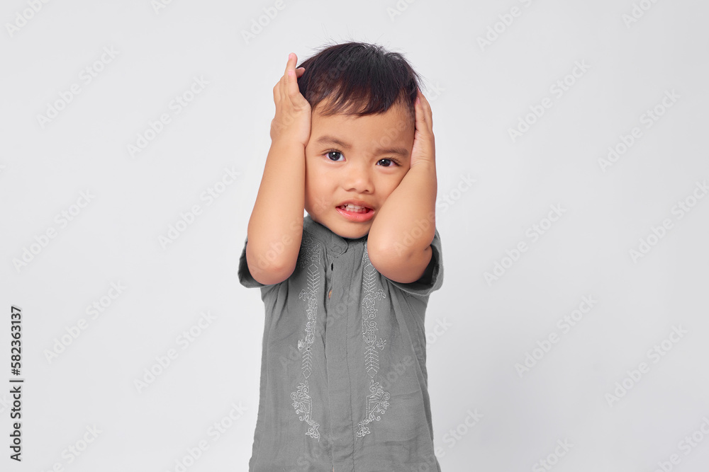 Unhappy toddler Asian muslim boy holding hand in head isolated on white studio background Unhappy toddler Asian muslim boy holding hand in head isolated on white studio background