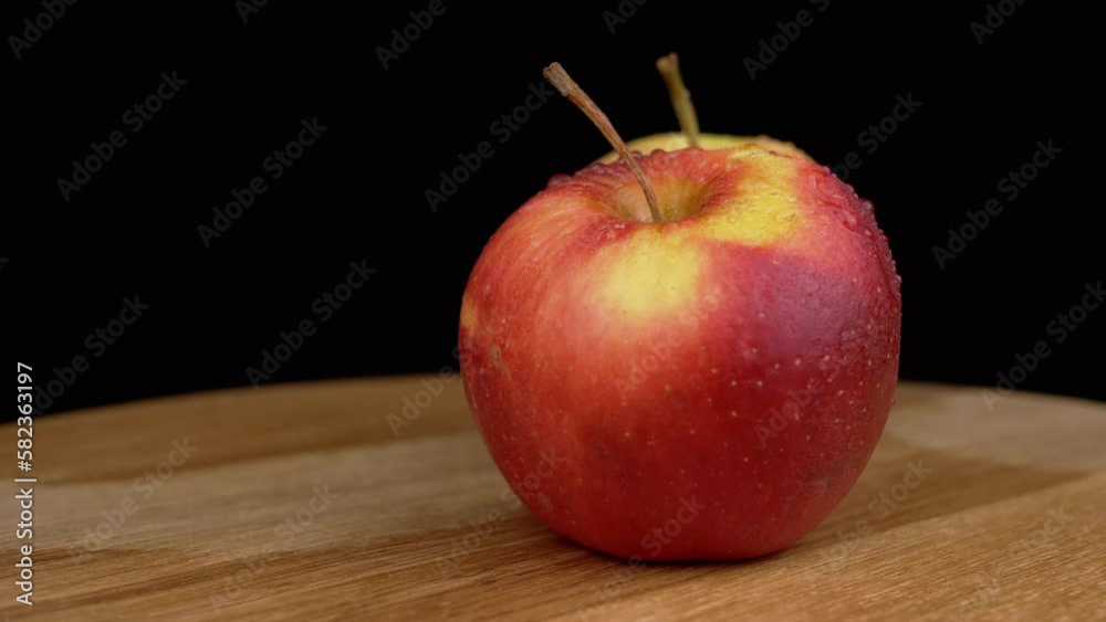 Two Ripe Red Apple with Water Drops on Peel Rotates on a Black Background. Golden and red apple color on wooden plate, cutting board. Fresh juicy apple on isolated background. Vitamins. Outer shine. Two Ripe Red Apple with Water Drops on Peel Rotates on a Black Background. Golden and red apple color on wooden plate, cutting board. Fresh juicy apple on isolated background. Vitamins. Outer shine.