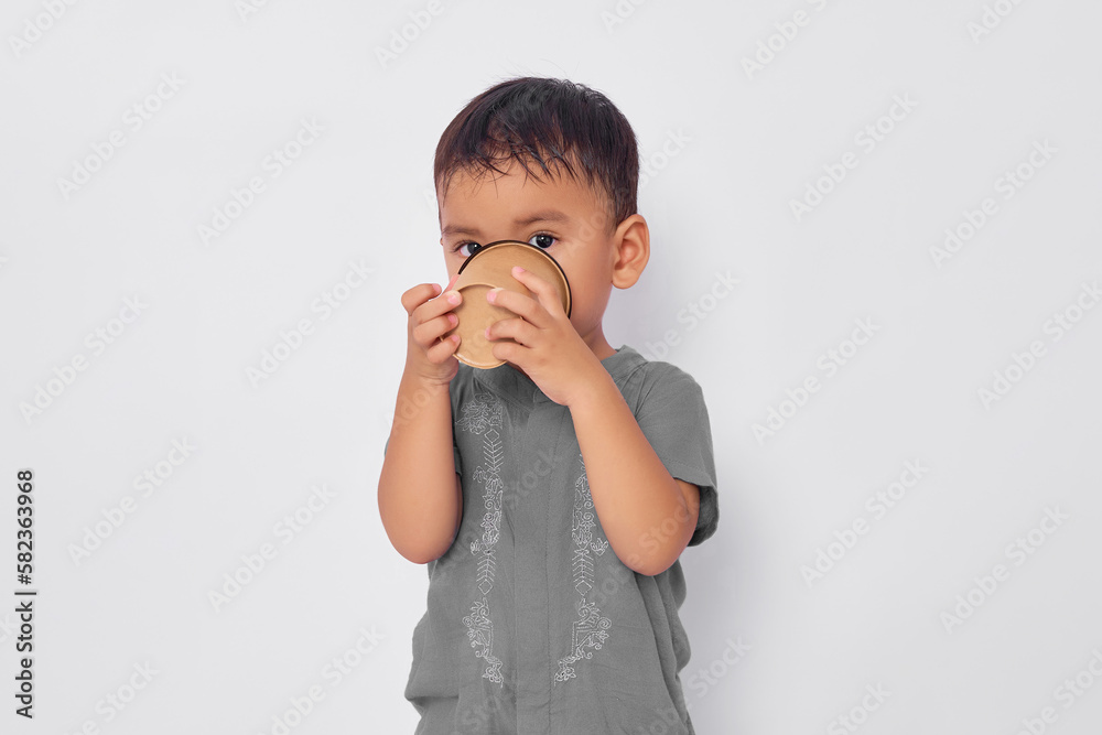 Smiling Asian muslim boy drinking water in paper cup isolated on white studio background