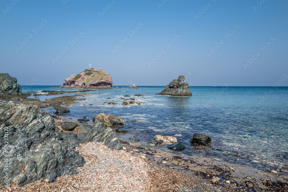 A beach by the sea with gravel and coarse boulders as well as a small island in the background.