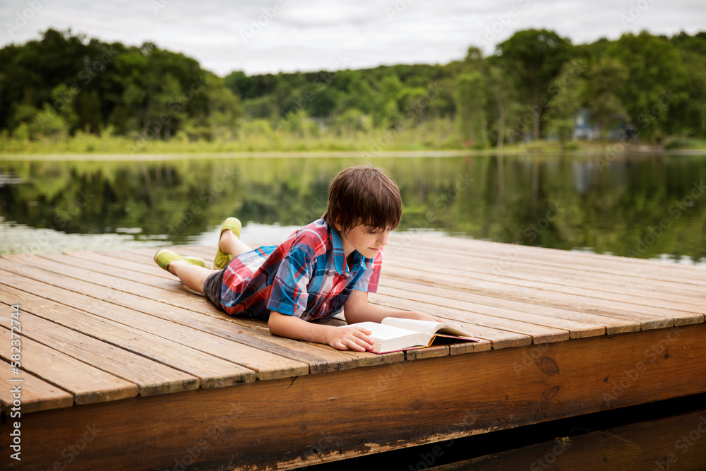Boy reading book while lying on dock Boy reading book while lying on dock