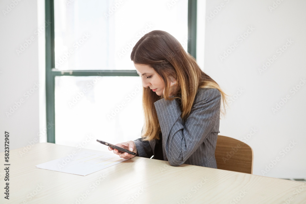 Businesswoman using smart phone at desk in creative office Businesswoman using smart phone at desk in creative office