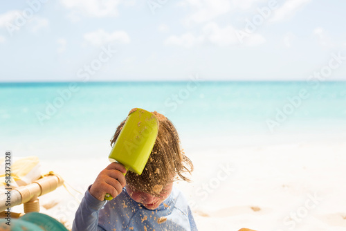 Boy pouring sand on head with toy shovel at beach photo