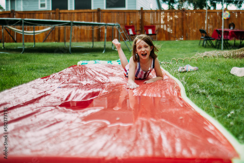 Young girl playing on slip and slide in back yard photo