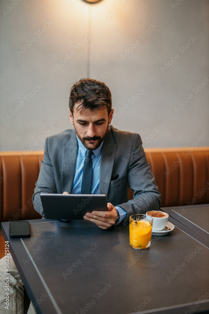 Focused smiling businessman sitting and working on his tablet in the bright lobby.