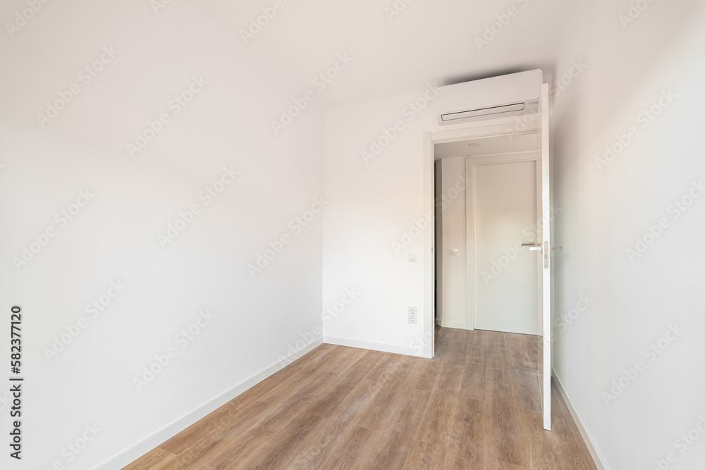 View of the front door to compact bright empty room without furniture with laminate flooring and with air conditioning. Concept of moving to a new apartment after building house