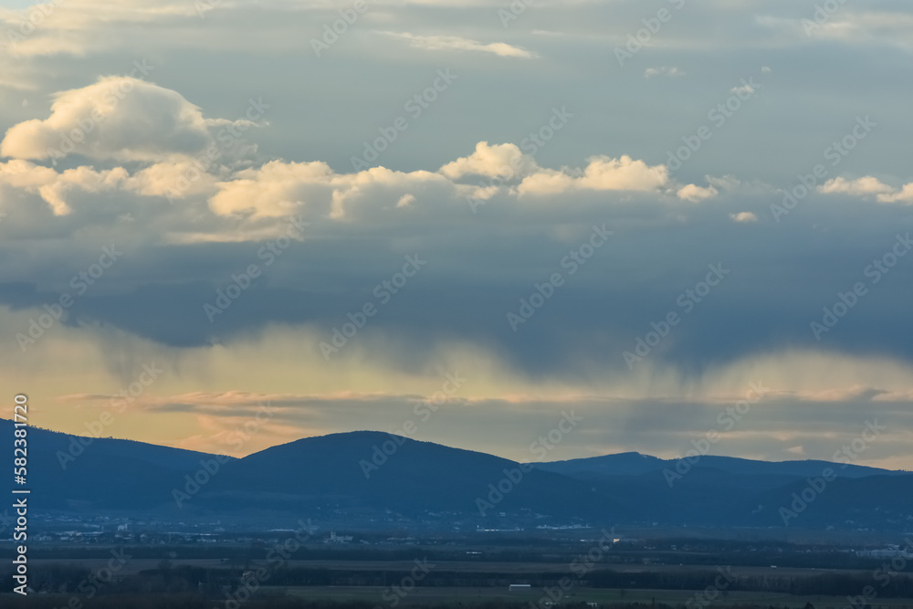 rain under clouds over a landscape with mountains