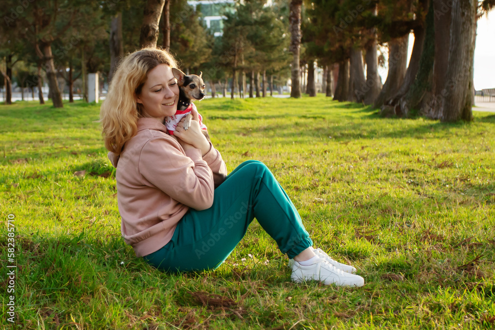 Fototapeta premium cute happy little dog in the hands of the owner in the summer in the park, the woman hugs the pet, protecting the pet from ticks