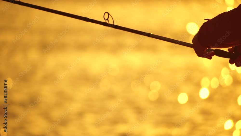 Man hobby fishing on sea tightens a fishing line reel of fish summer. Calm surface sea. Close-up of a fisherman hands twist reel with fishing line on a rod. Fishing in the sea outdoors. Slow motion. Man hobby fishing on sea tightens a fishing line reel of fish summer. Calm surface sea. Close-up of a fisherman hands twist reel with fishing line on a rod. Fishing in the sea outdoors. Slow motion.