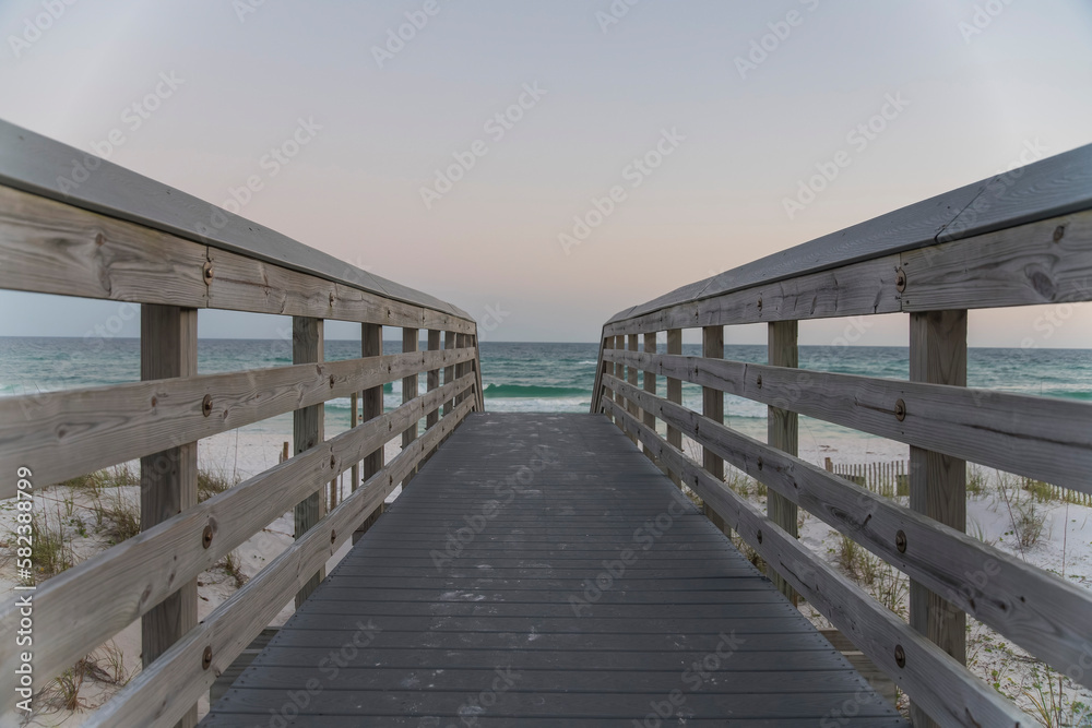 Obraz premium Straight pathway to the beach with horizon skyline background at Destin, Florida. Walkway over the fenced sand dunes near the white sand shore.