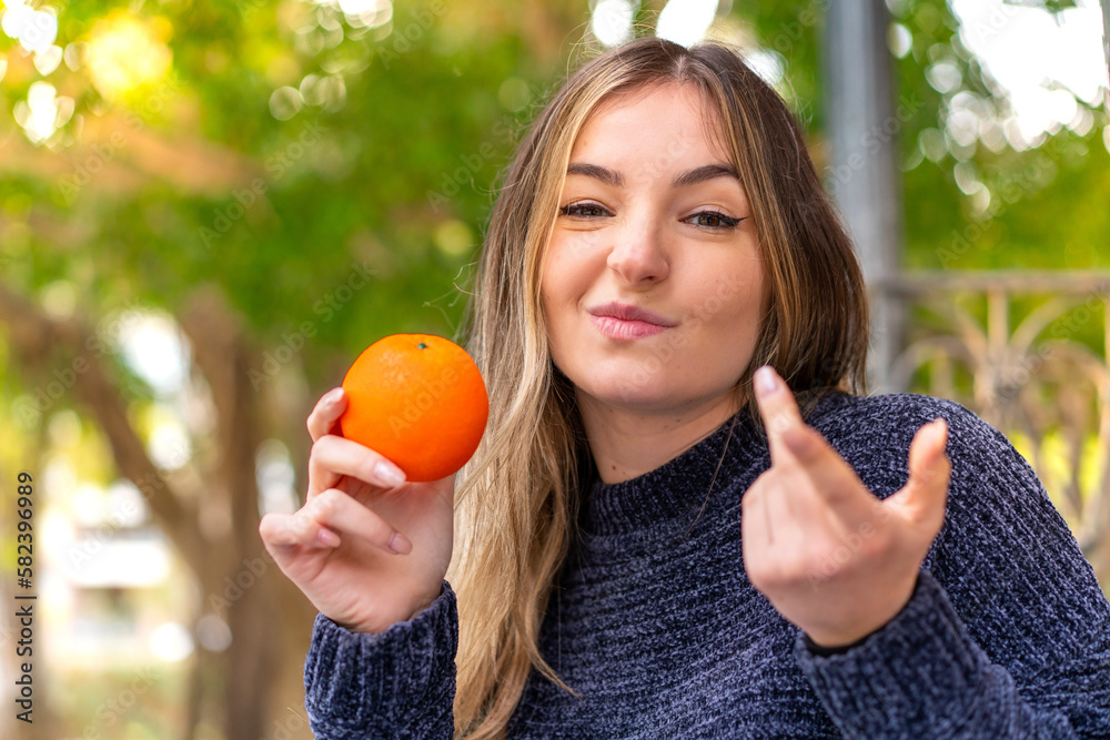 Young pretty Romanian woman holding an orange at outdoors making doubts gesture while lifting the shoulders Young pretty Romanian woman holding an orange at outdoors making doubts gesture while lifting the shoulders