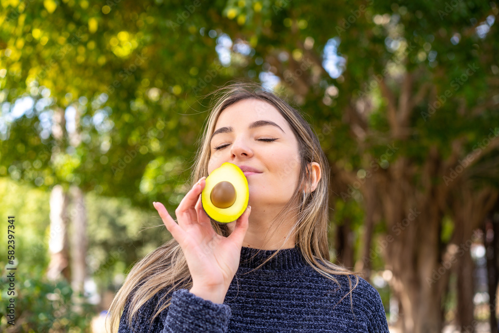 Young pretty Romanian woman holding an avocado at outdoors Young pretty Romanian woman holding an avocado at outdoors