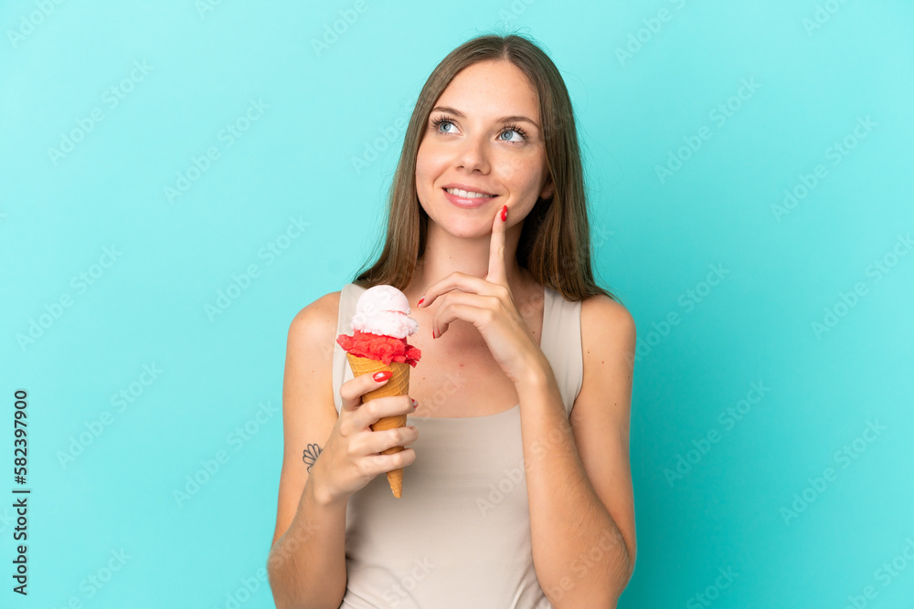 Young Lithuanian woman with cornet ice cream isolated on blue background thinking an idea while looking up Young Lithuanian woman with cornet ice cream isolated on blue background thinking an idea while looking up
